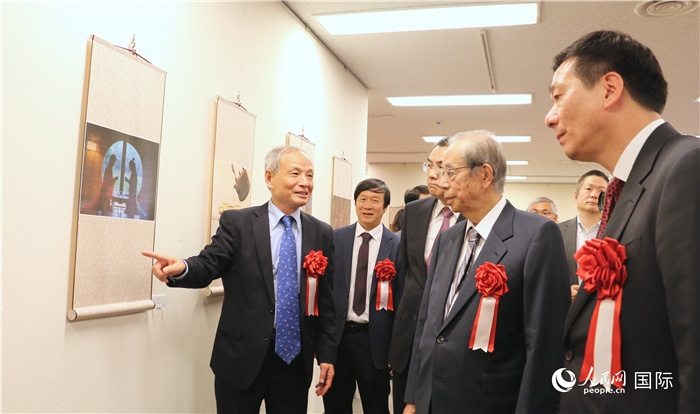 “湖州印象”攝影展主創(chuàng)、世界華人攝影協(xié)會(huì)副會(huì)長(zhǎng)馮學(xué)敏向吳江浩大使、福田康夫前首相等嘉賓介紹展出作品。（人民網(wǎng) 許可攝）
