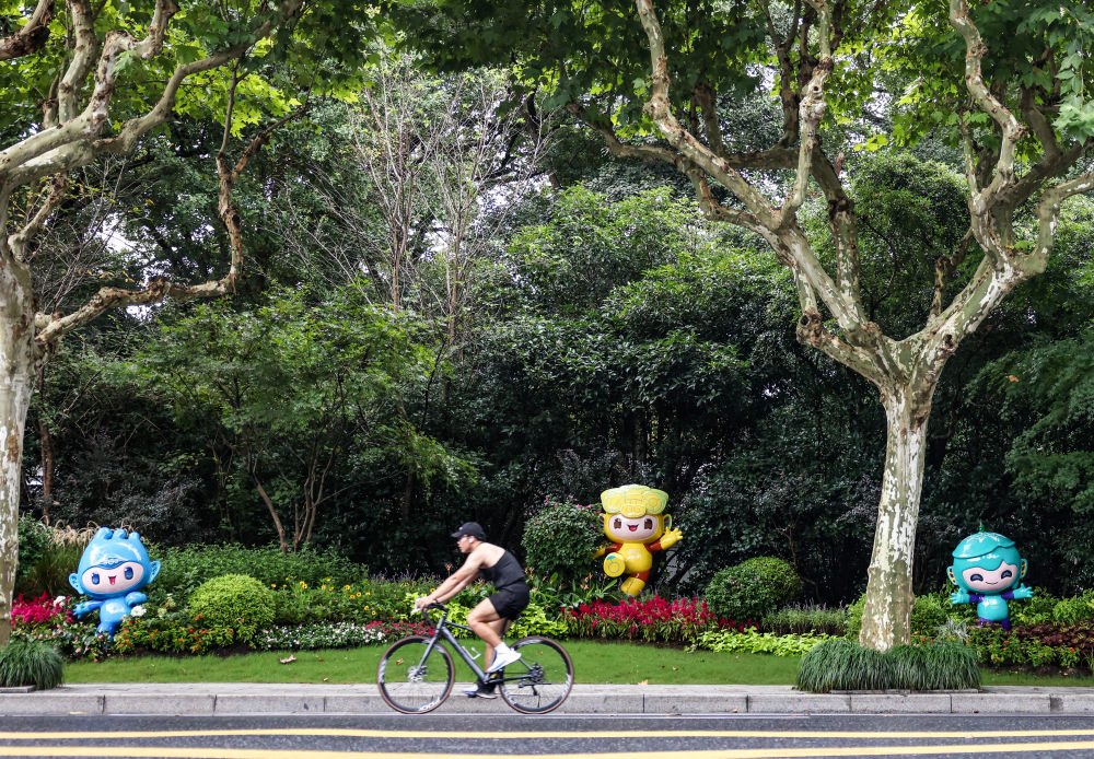市民在杭州市南山路上一處亞運會主題吉祥物雕塑前騎自行車。