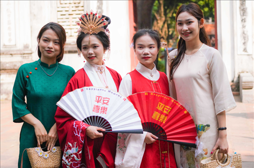身穿古裝的中國游客和身穿越南傳統(tǒng)服飾奧黛的越南青年在文廟門前合影。
