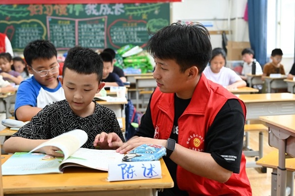 鄭州市二七區(qū)暑托班的志愿者輔導(dǎo)孩子寫作業(yè)。人民網(wǎng)記者王玉興攝