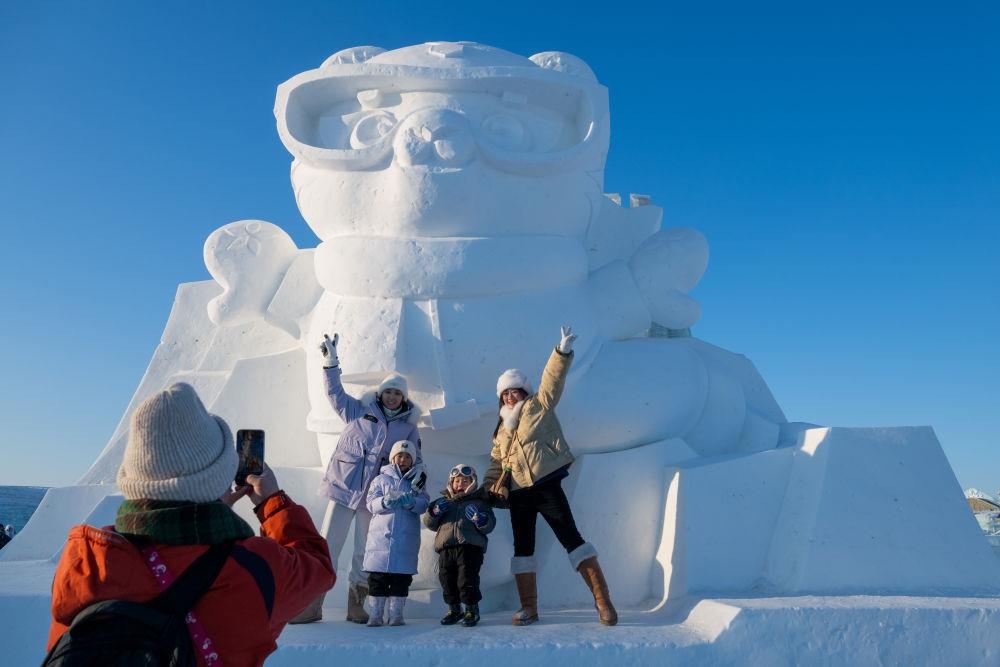 2025年1月3日，在黑龍江哈爾濱冰雪大世界園區(qū)，游客與亞冬會吉祥物雪雕“濱濱”合影